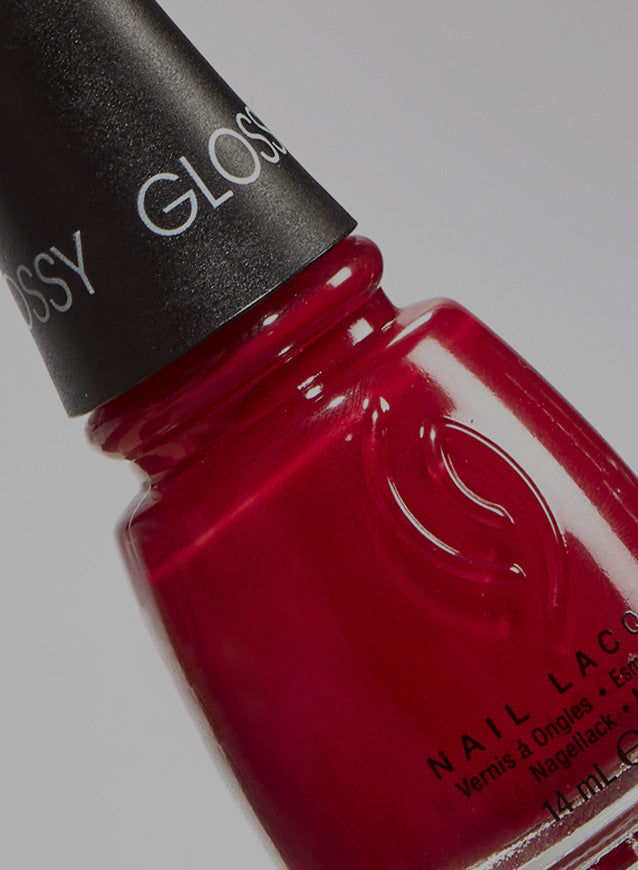 Close-up of a red nail lacquer bottle with 'Glossy' branding on a gray background