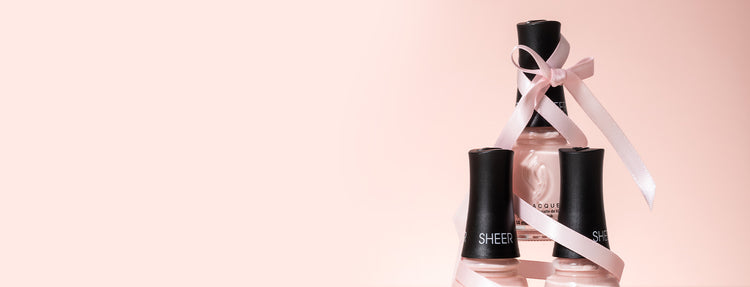 Three nail polish bottles with ribbons on a pink background