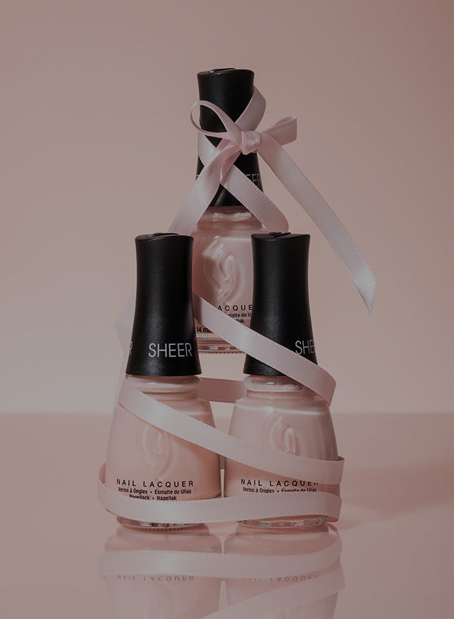 Three bottles of nail lacquer with a ribbon on a pink background
