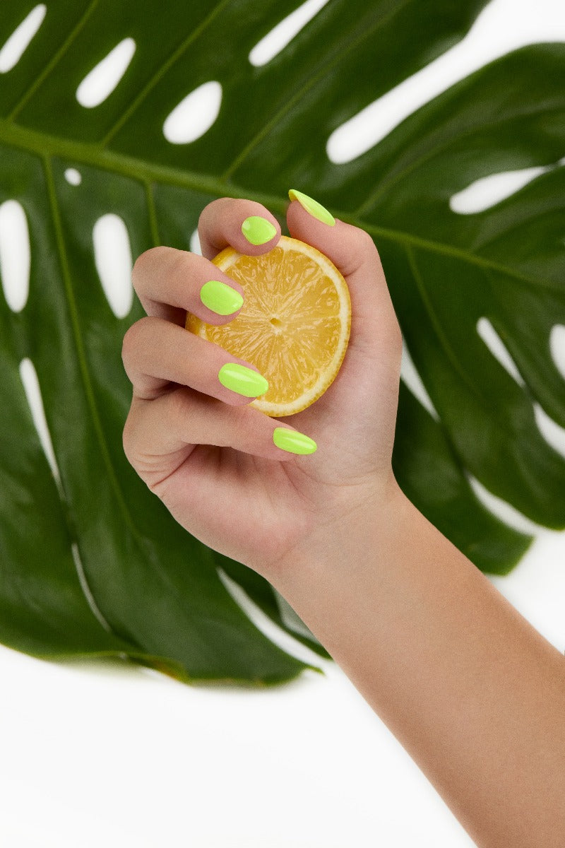 A woman with medium skin tone holding citrus lemon revealing her almond-shaped colored nails